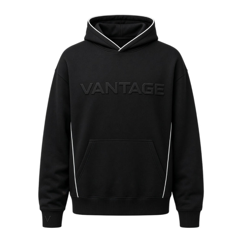 A black pullover hoodie with 'VANTAGE' printed across the chest in a tonal dark gray font, featuring white piping details along the hood, sides, and front pocket.