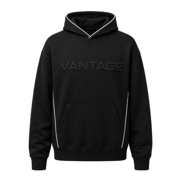 A black pullover hoodie with 'VANTAGE' printed across the chest in a tonal dark gray font, featuring white piping details along the hood, sides, and front pocket.